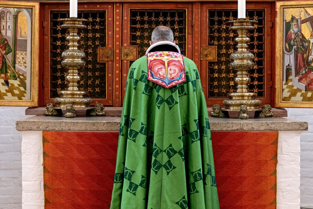 Biskop iført grøn bispekåbe designet af Dronning Margrethe i Aarhus Domkirke. På ryggen ses broderede symboler for tro, håb og kærlighed - kors, anker og hjerte.
