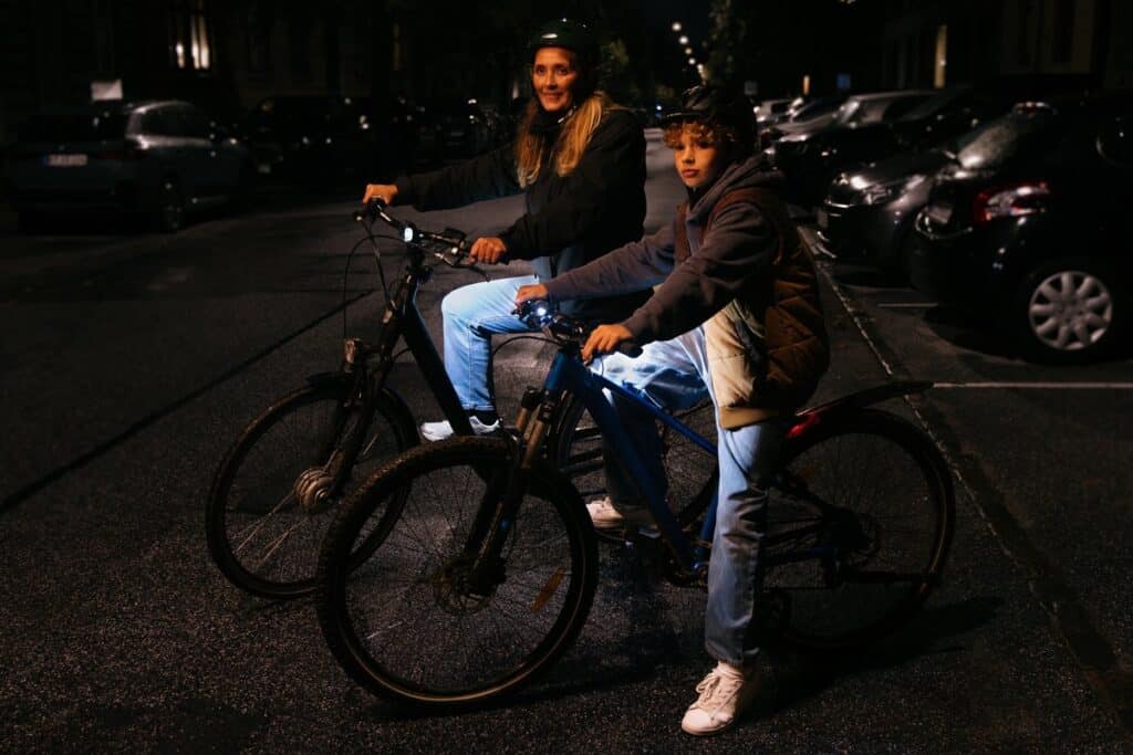 Mor og son cykler i morke med lys pa benene og cykelhjelm